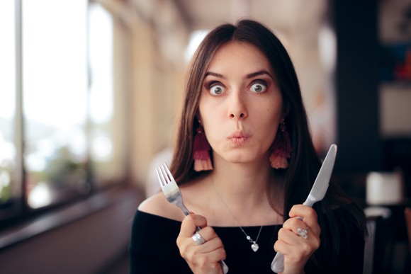 A person in a restaurant holding a fork and knife.