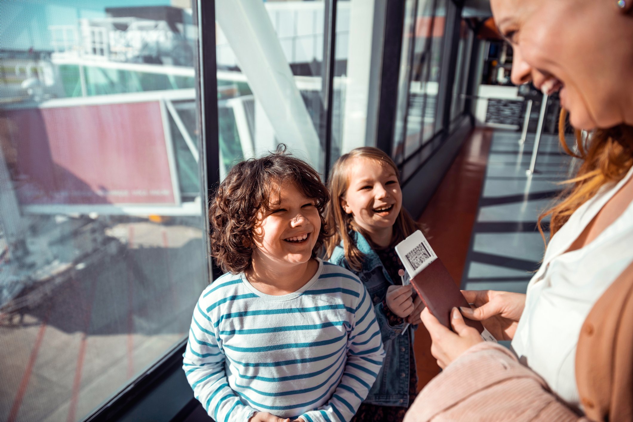 A person holding two boarding passes is seen smiling with two children in an airport. 