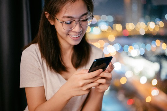A smartphone user stands by a window at night.