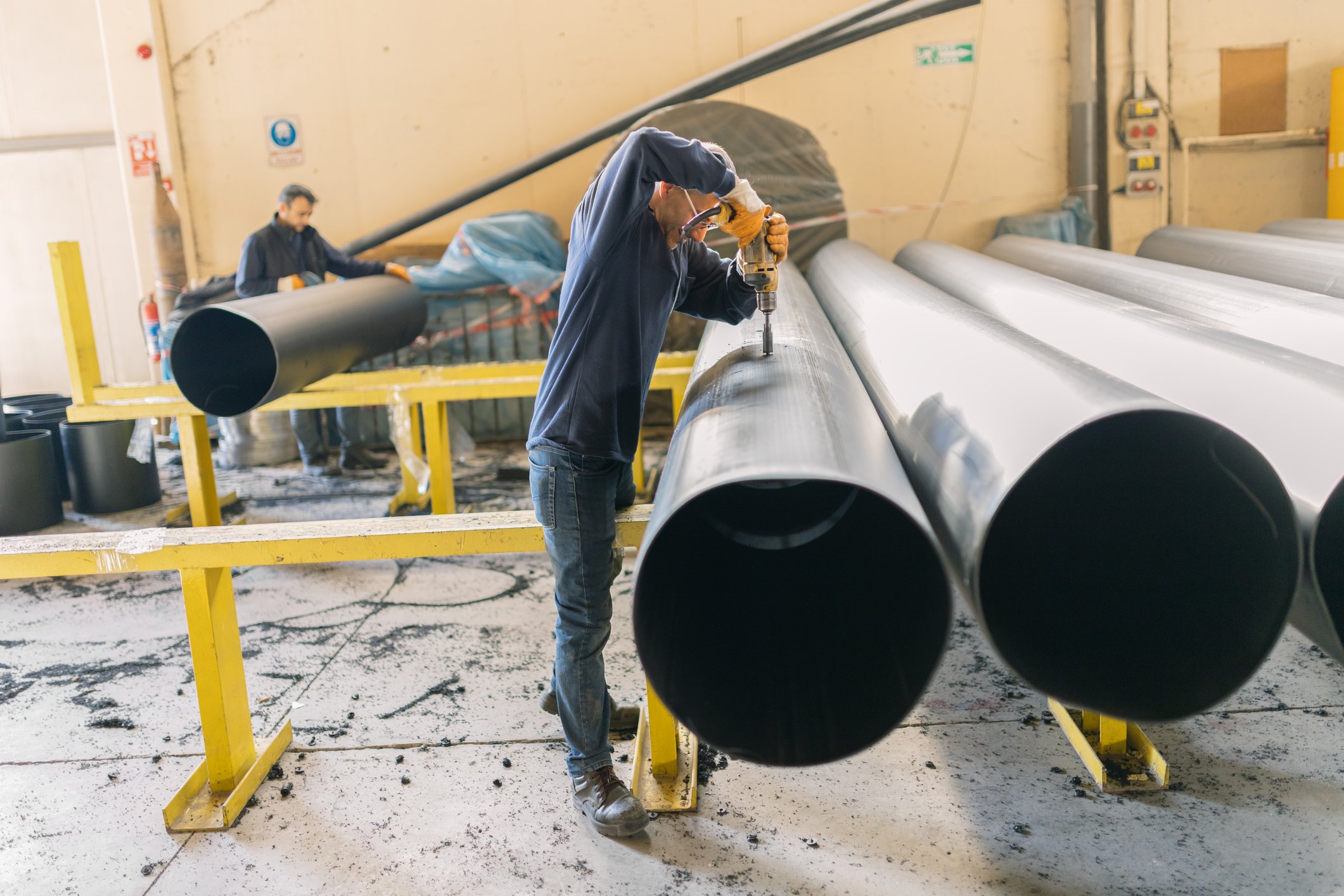 Men work on a big pipe in a factory.