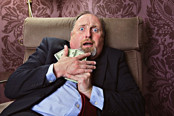 Scared person sitting in arm chair holding onto money.