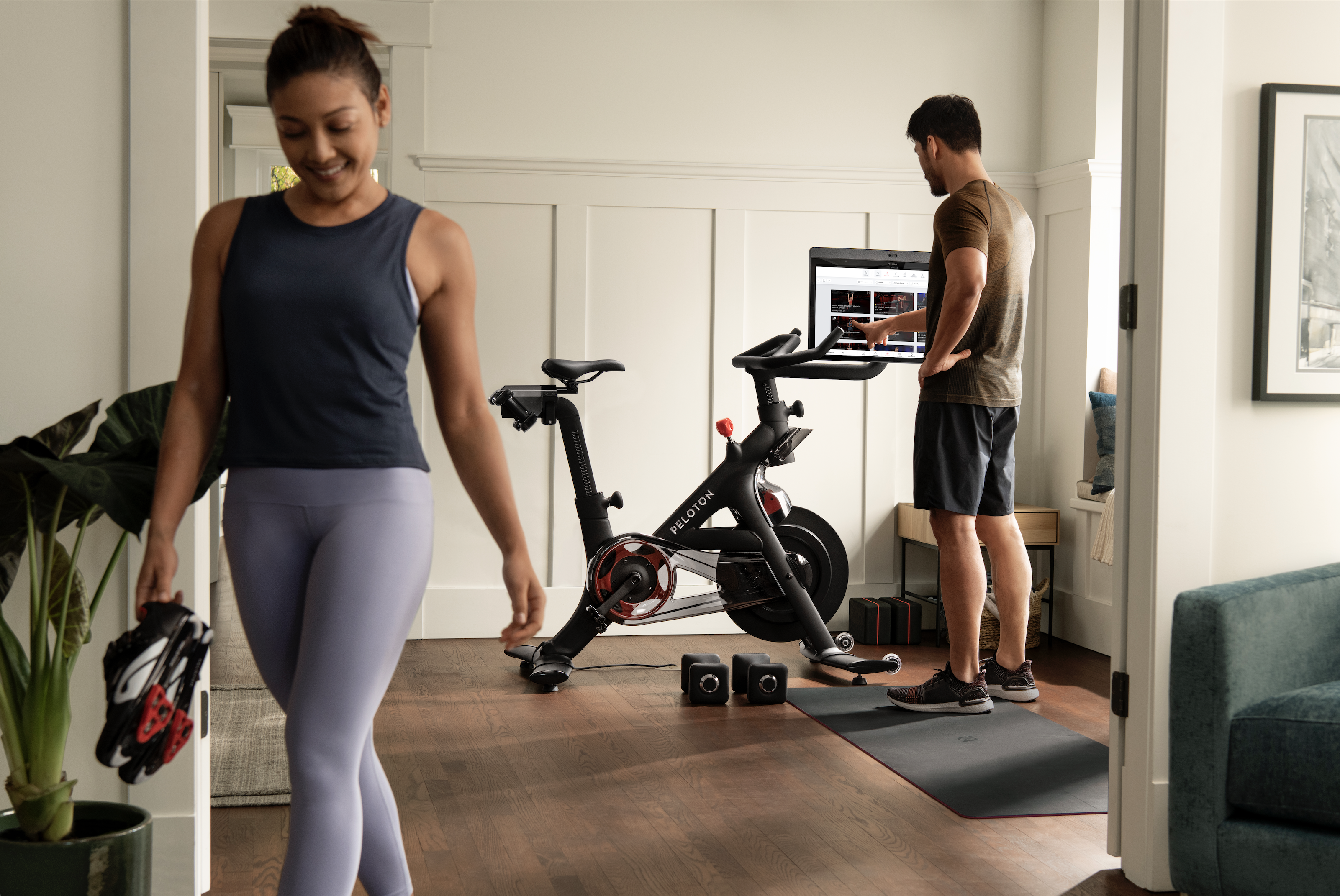 Two people in workout clothes take turns using a Peloton bike.