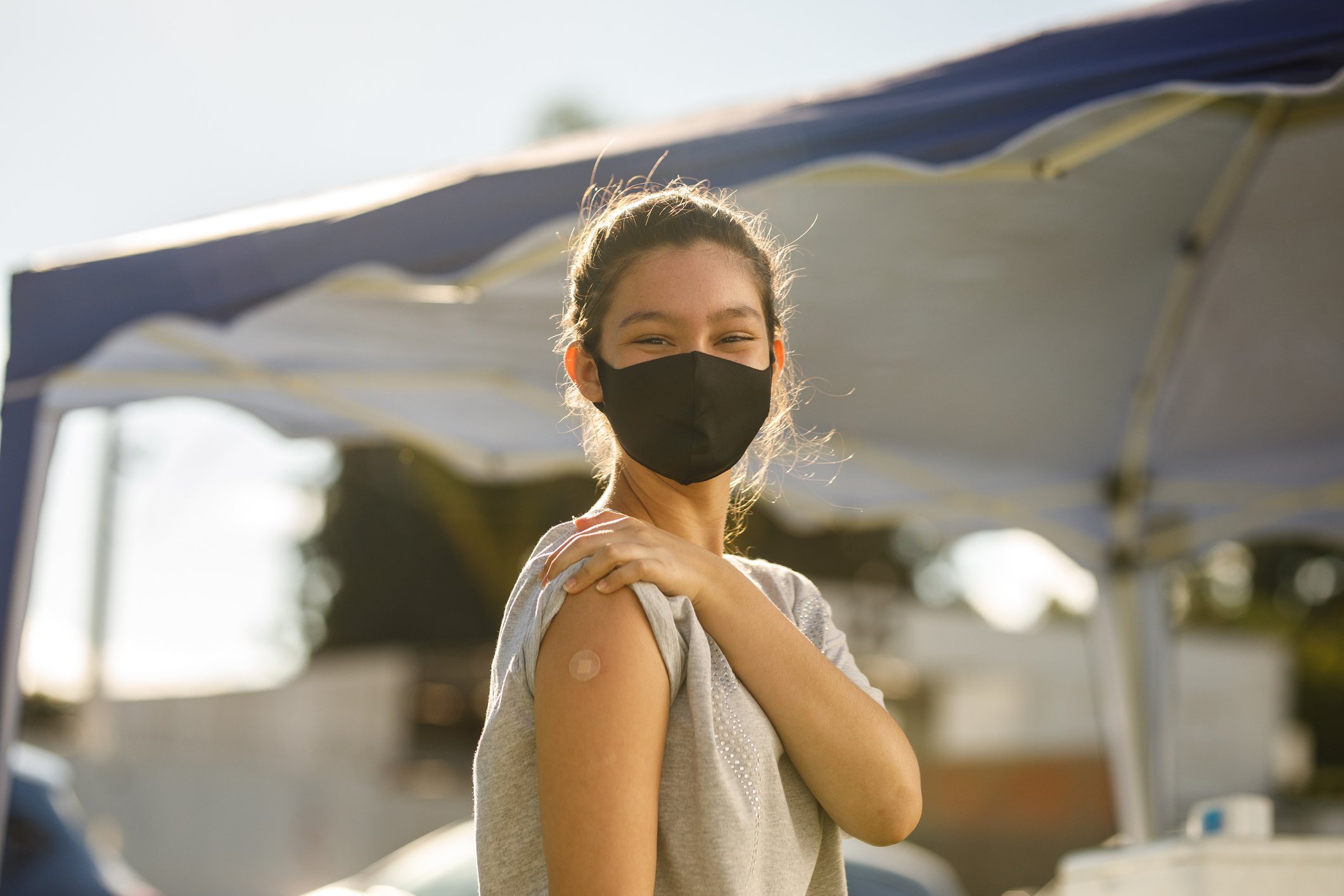 A teenage girl displays here vaccine sticker at a health center while wearing a mask.