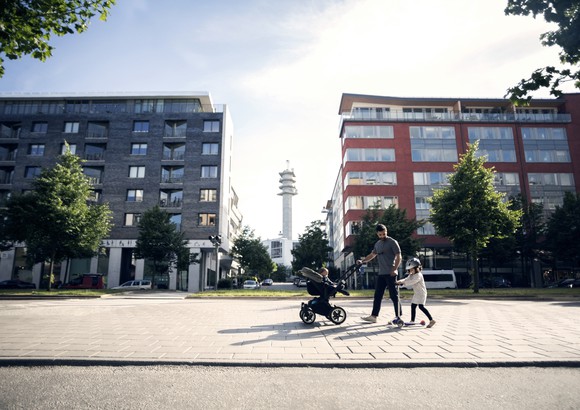 An adult walks with two children in front of apartment buildings.