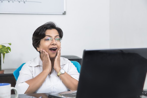A woman is pleasantly surprised by what she sees on a computer screen.