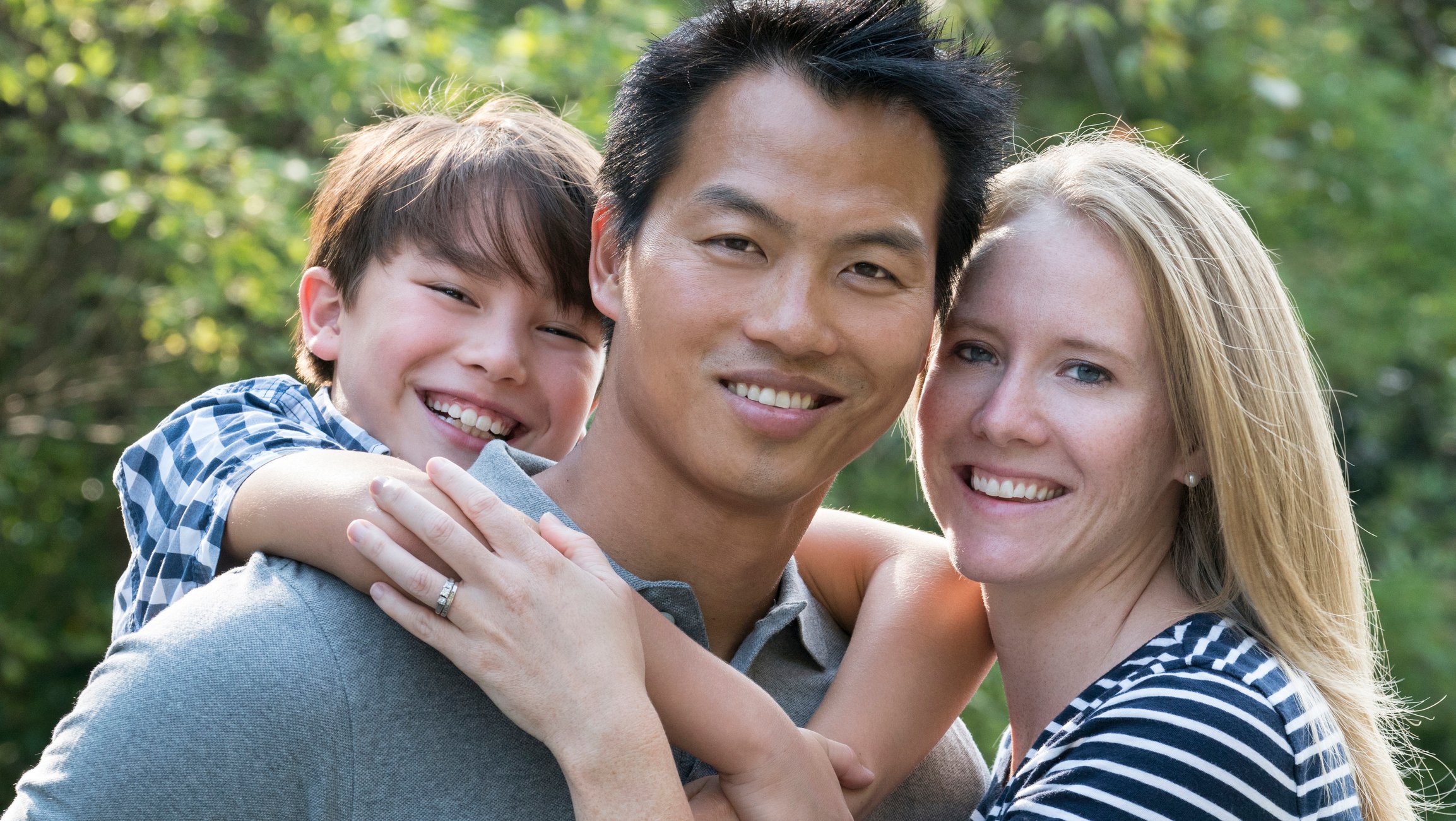 Two smiling adults and a smiling child holding on to each other.