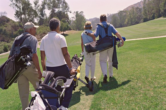 foursome of golfers carrying bags with clubs on a golf course.