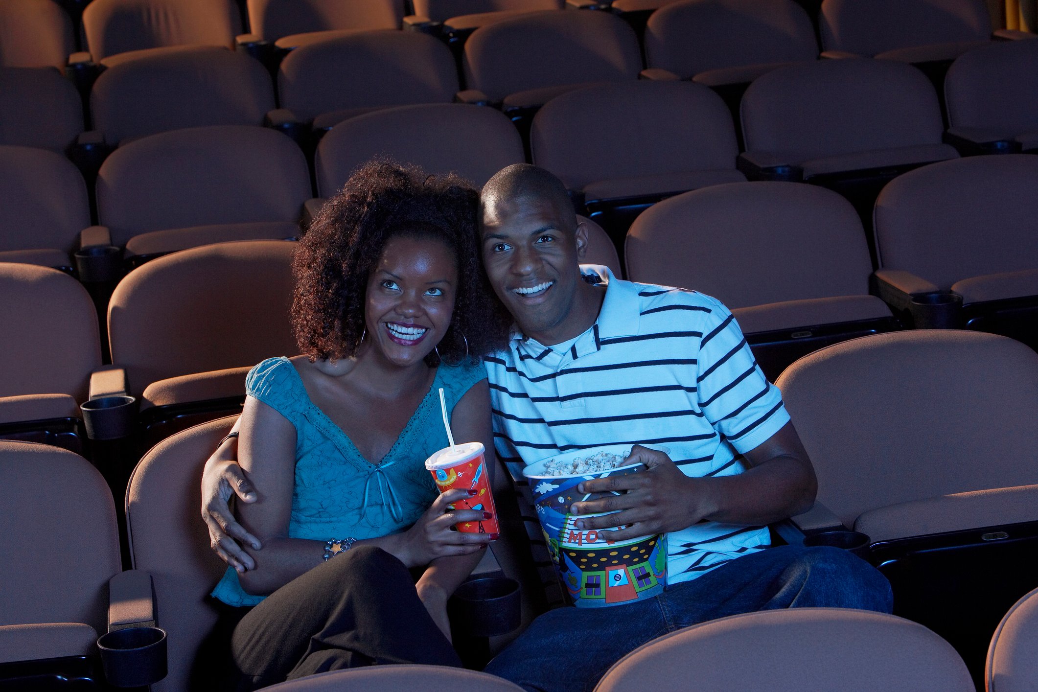 A couple smile and enjoy snacks while watching a movie in a theater.