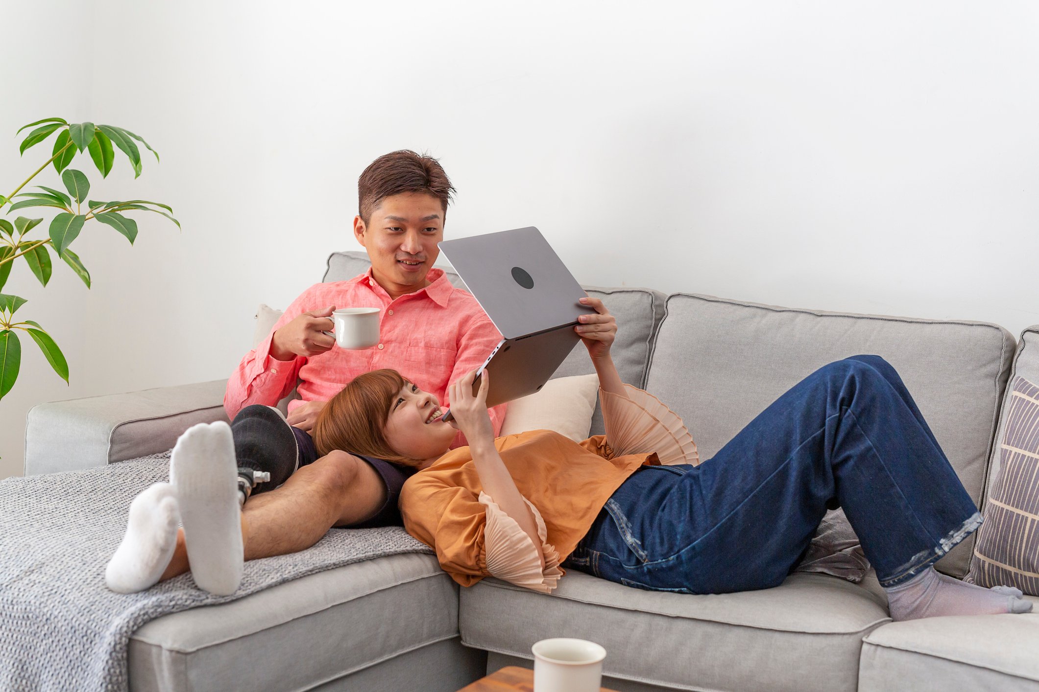 Couple lies on couch while looking at laptop.
