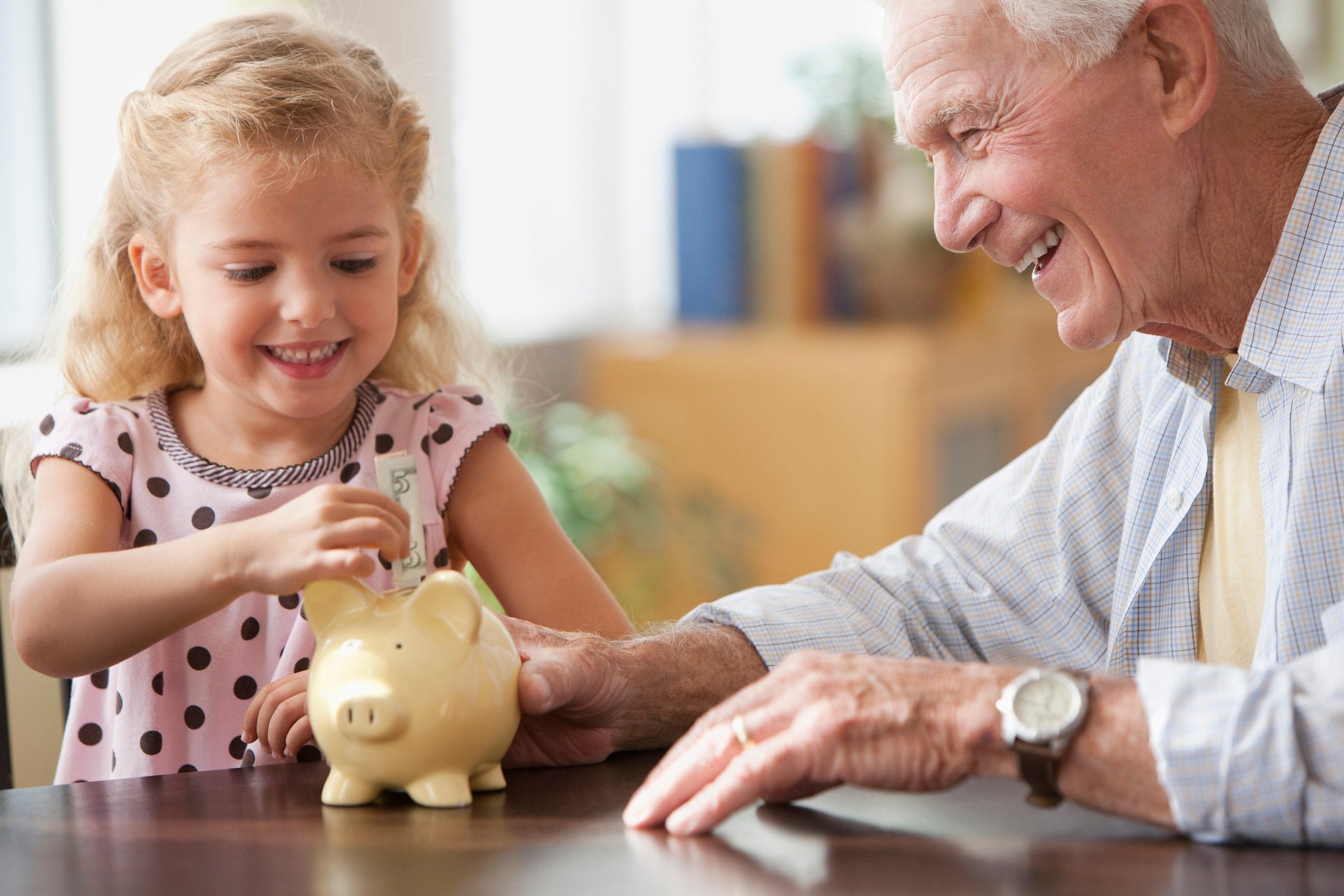 Smiling grandparent and grandchild putting money in piggy bank.