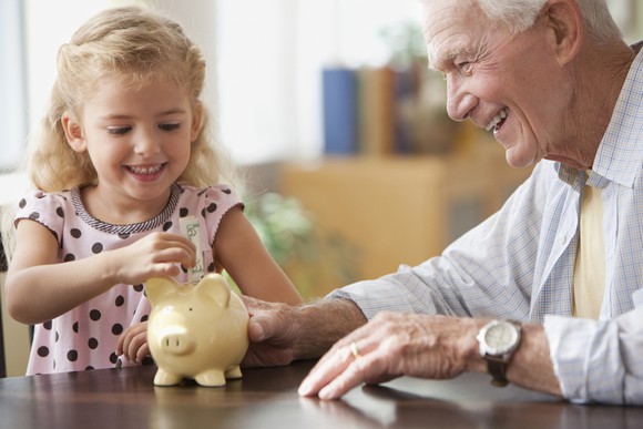 Smiling grandparent and grandchild putting money in piggy bank.