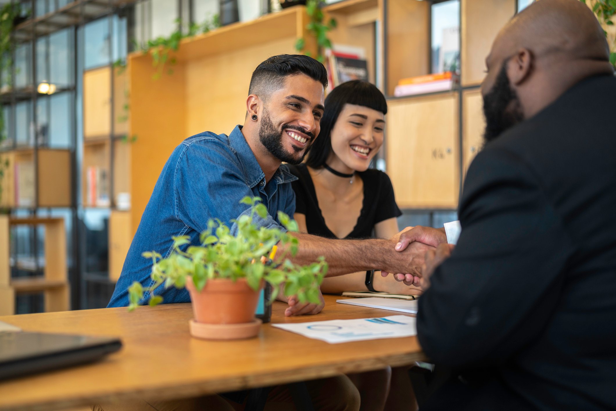 A smiling couple shaking hands across a desk with a lender.