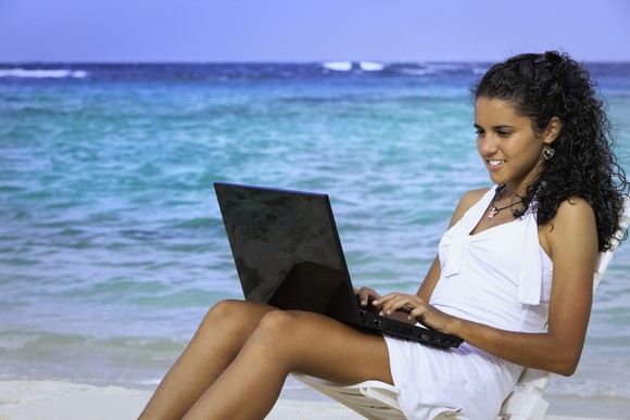 Smiling person sitting in a chair on the beach with a laptop.