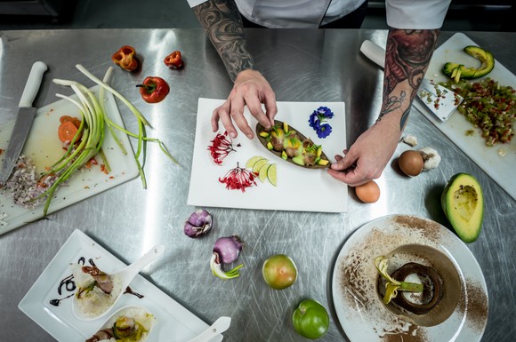 A chef with tattoos working with fruit and vegetables. 