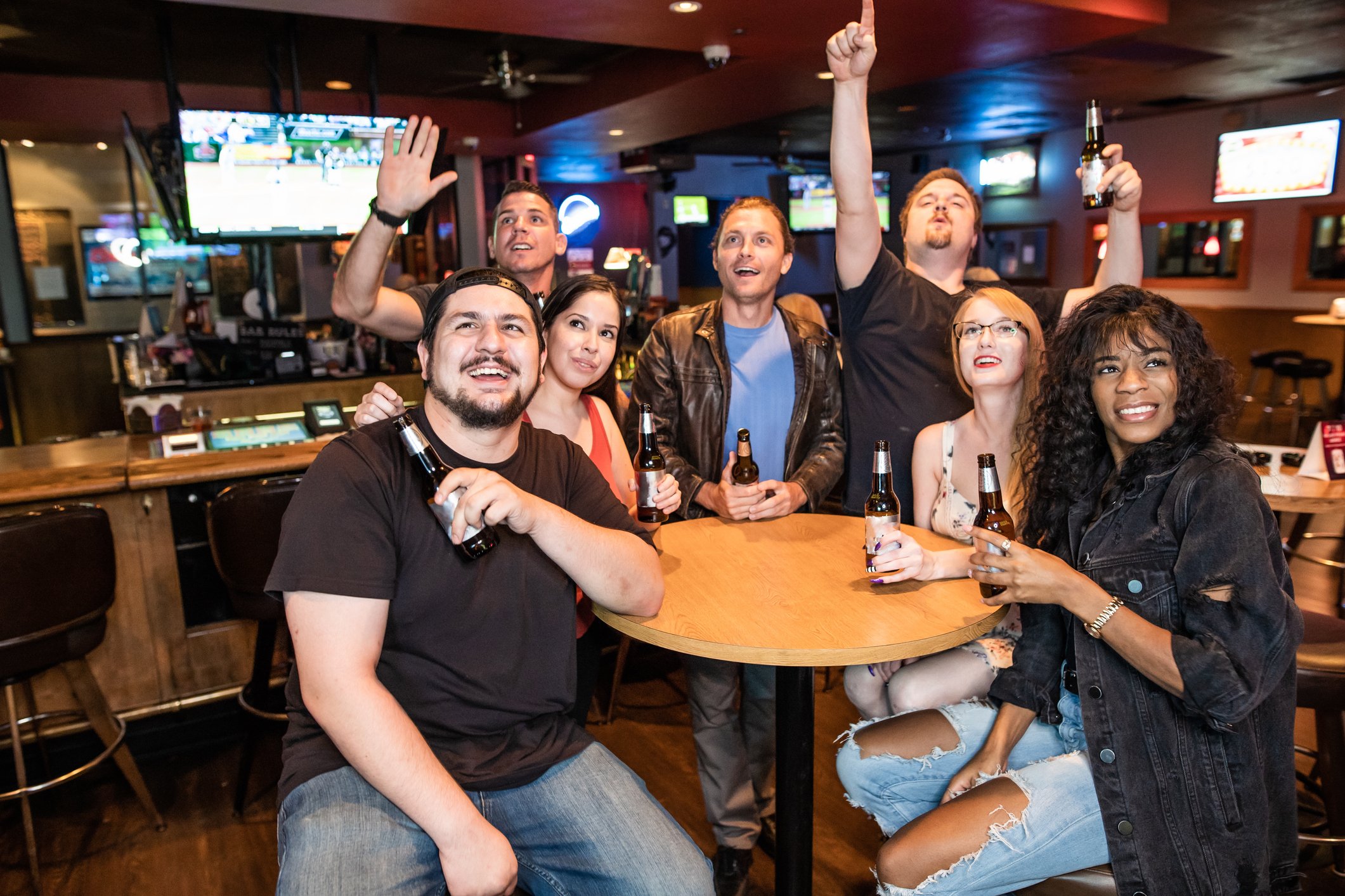 a group of people cheer while sitting around a table holding drinks in a sports bar