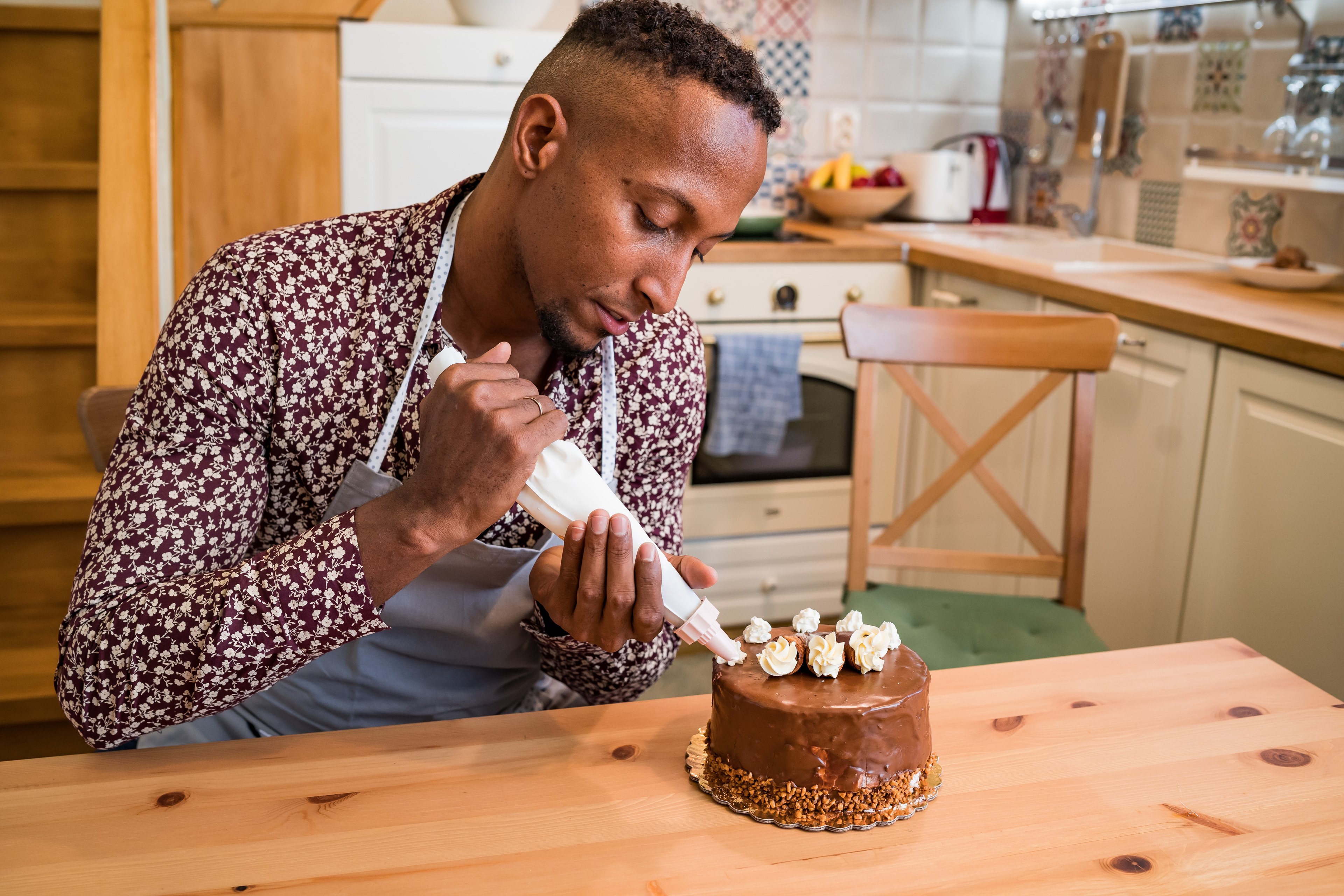 A baker puts icing on a cake in a home kitchen.