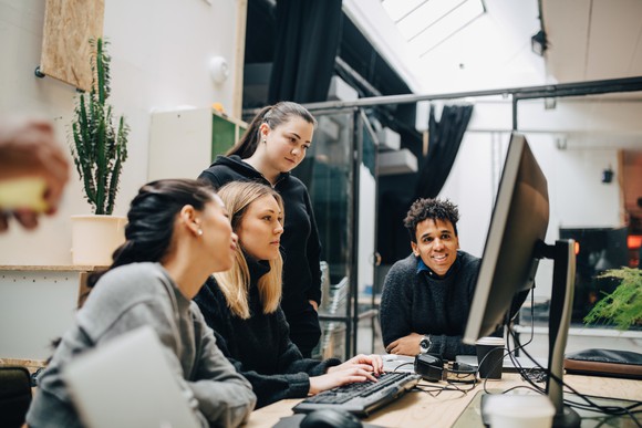 Four people work together in front of a computer.