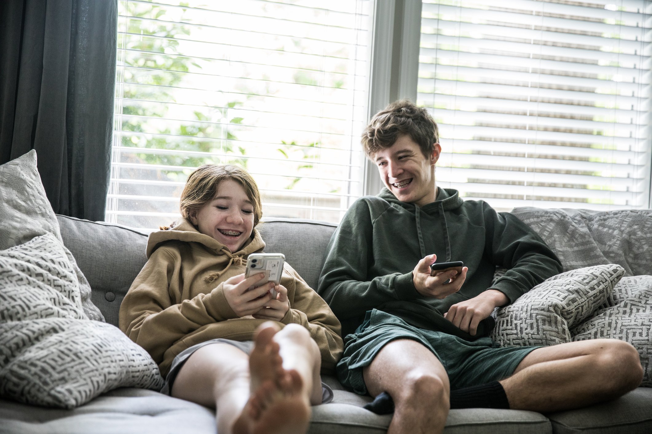 Two teenagers holding smartphones sitting on a couch.