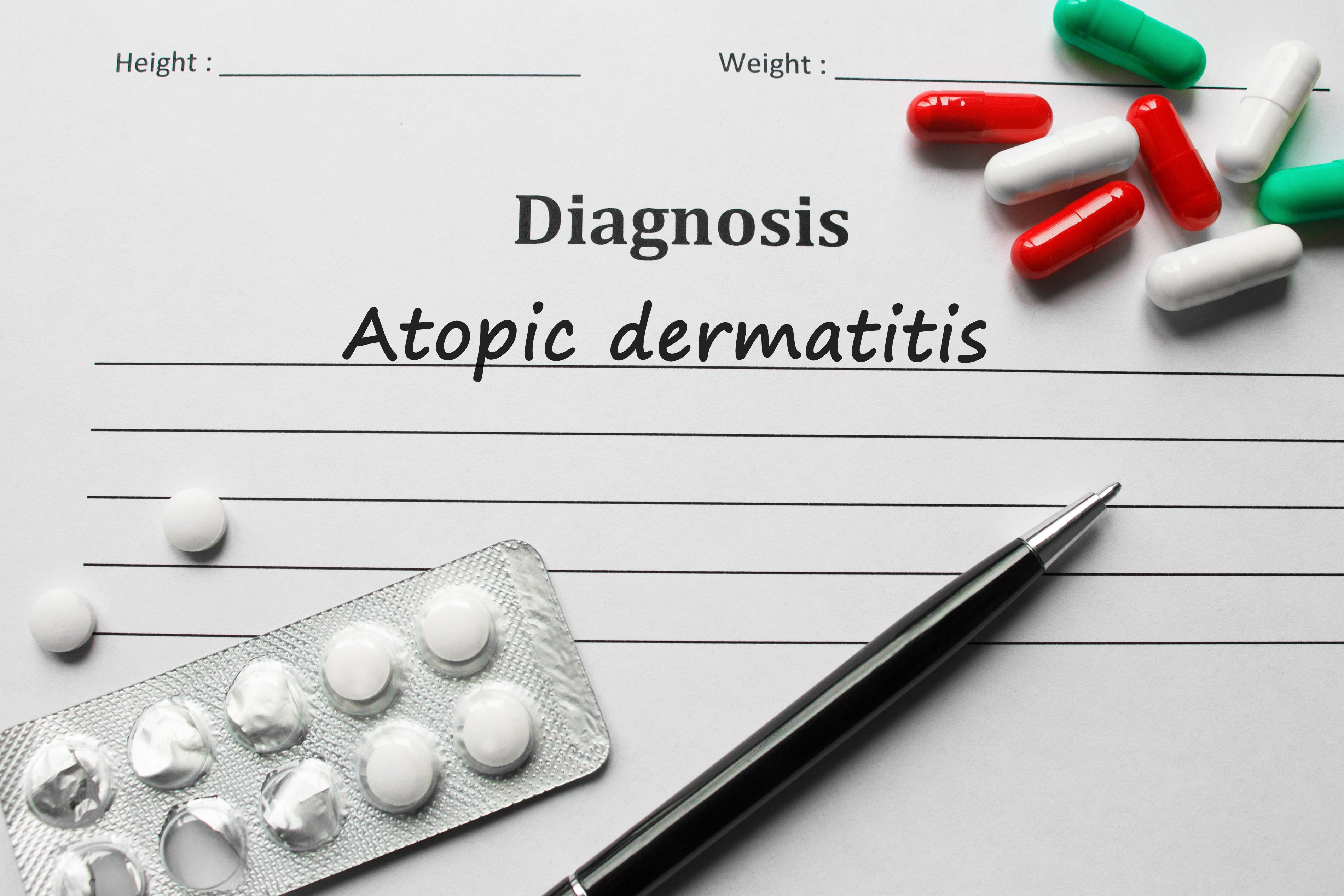 Document with atopic dermatitis printed underneath a Diagnosis heading with several pills and a pen on top of the document.