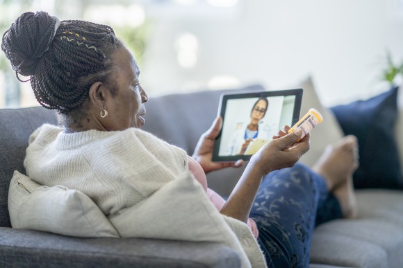 A patient lying on a sofa conducting a virtual visit with a doctor on a tablet.