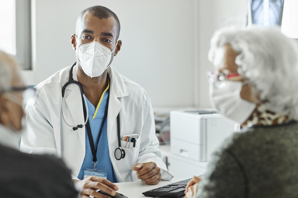 Two people seated and talking to a doctor who is seated across from them.