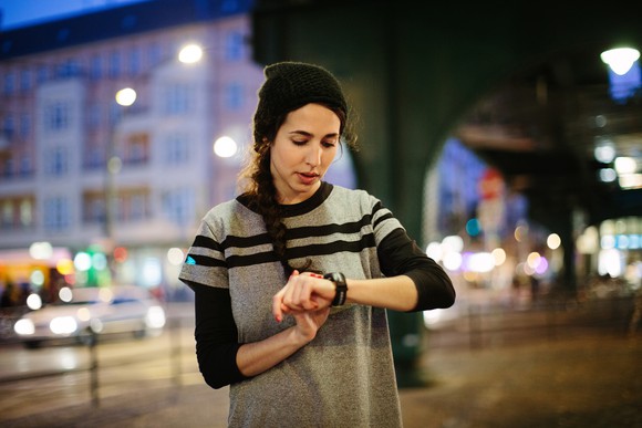 A young woman checks a smartwatch in a city at night.