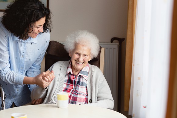 An older person seated and smiling being cared for by another person standing alongside.