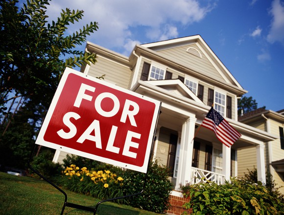 Beige home with a "For Sale" sign in the front yard.