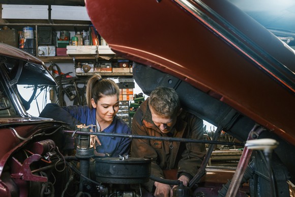 A woman and a man working on a car.