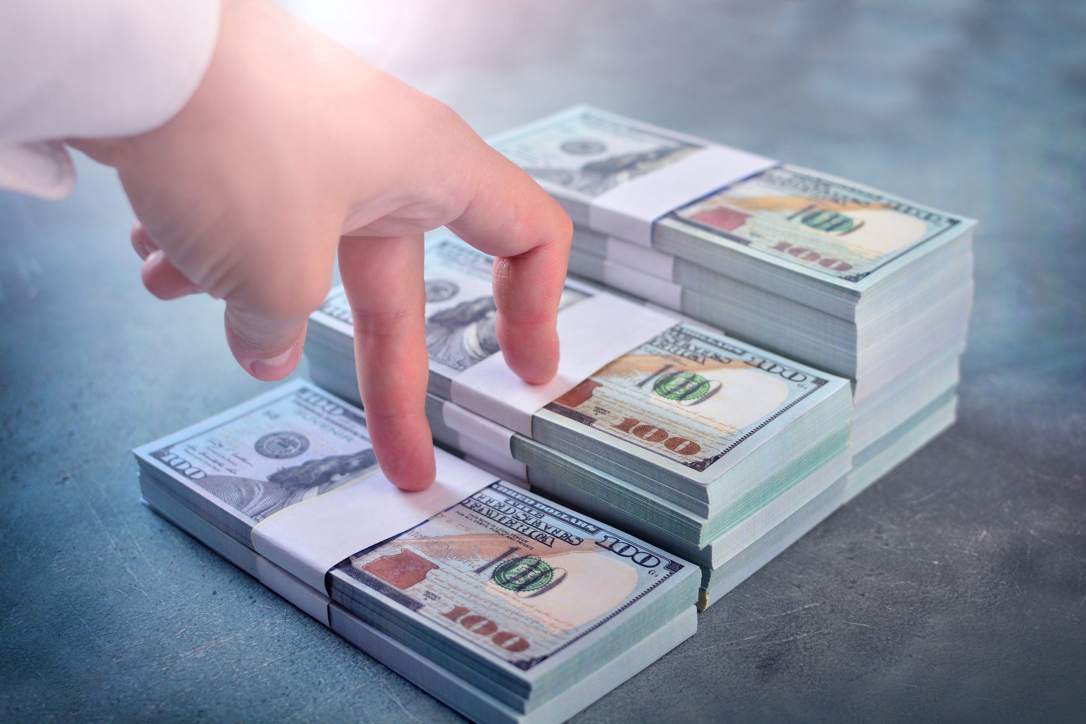 Fingers on a hand step up a stair-step pile of $100 bills