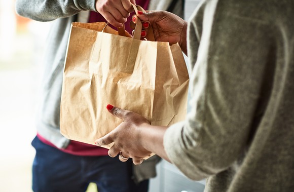 One person handing another a paper bag.