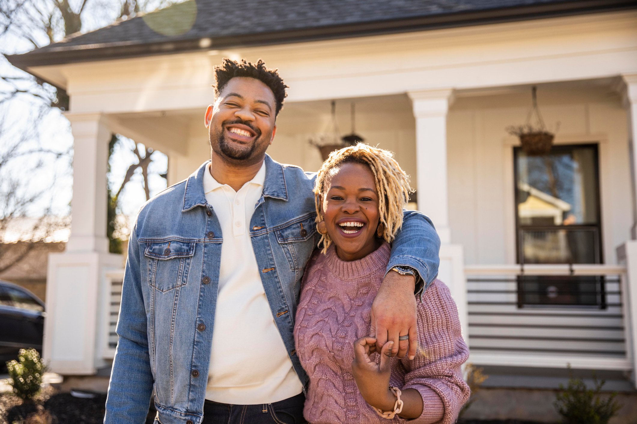 Adult couple smiling in front of home.