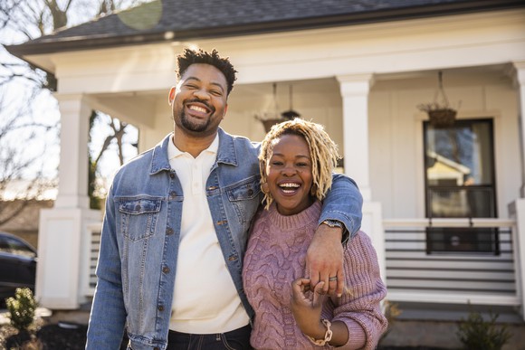 Adult couple smiling in front of home.