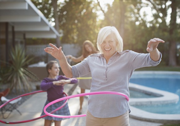 A senior using a hulu hoop next to their family by a pool.