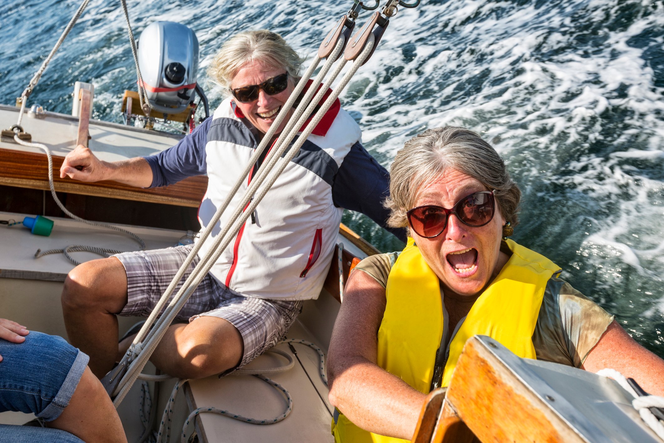 A man and woman in a sailboat react as the boat tips to the side. 