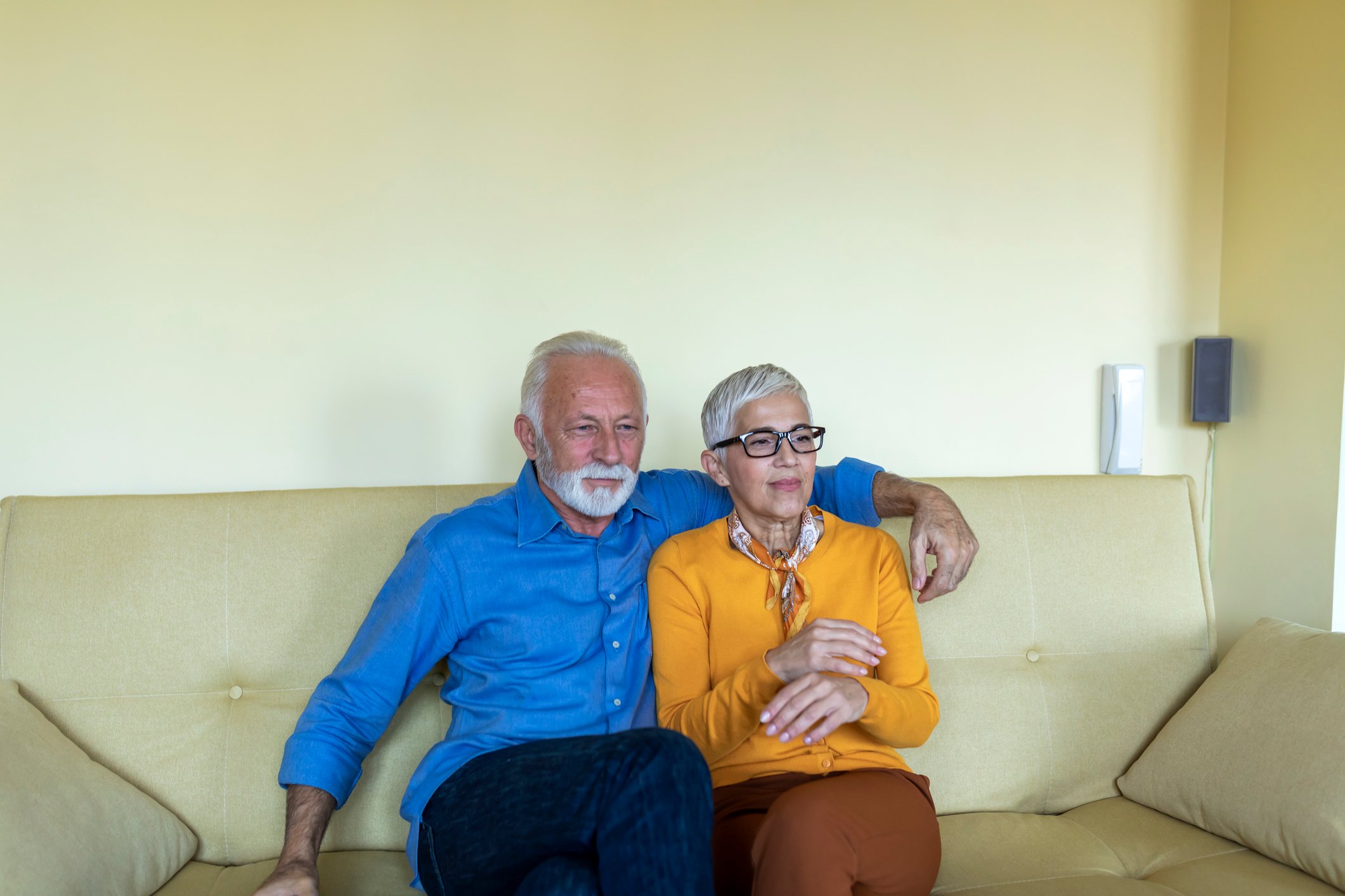 Two older people sitting together on a couch watching something.