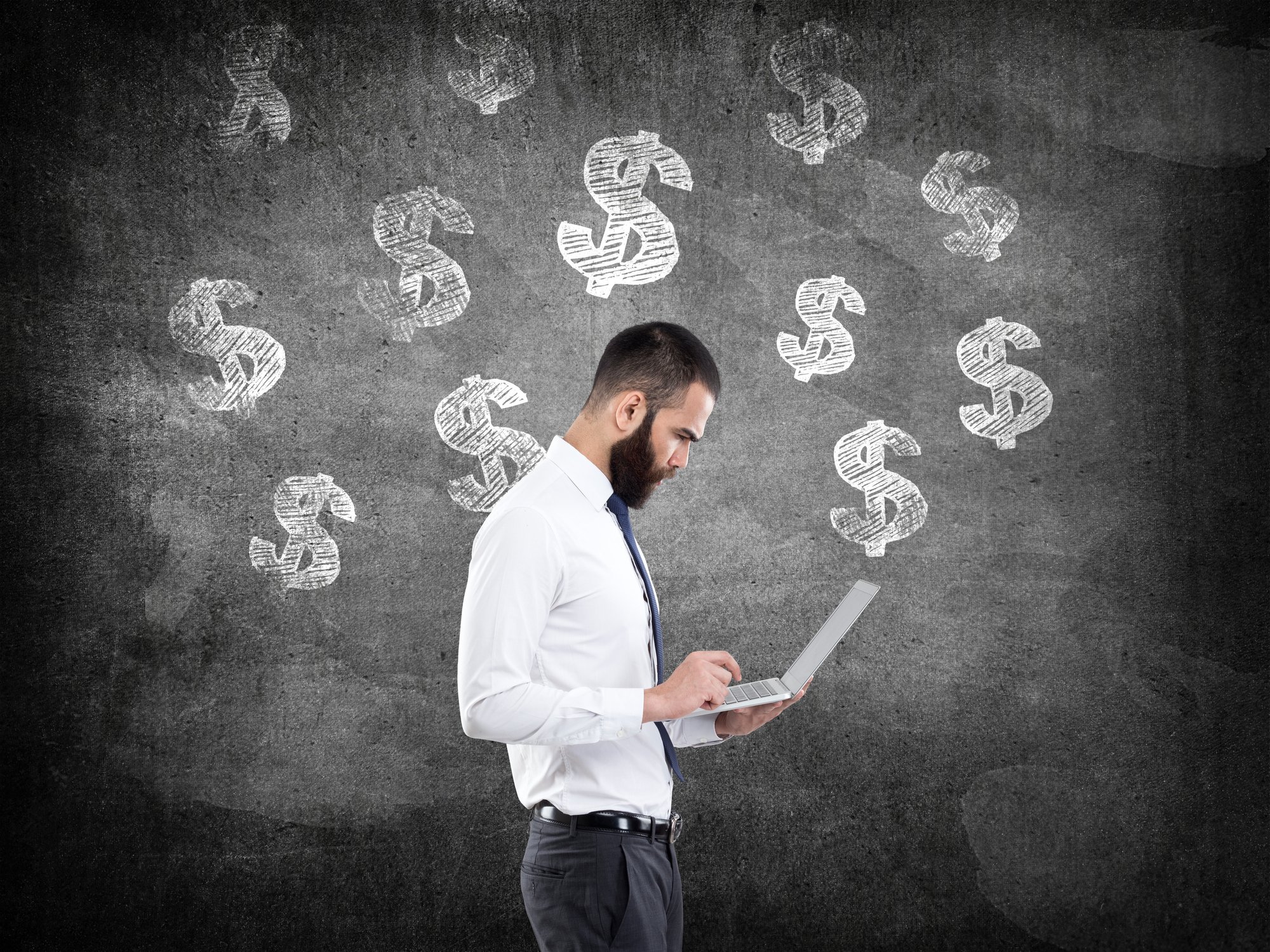 Dollar signs drawn on a board behind a person looking at a laptop while standing.