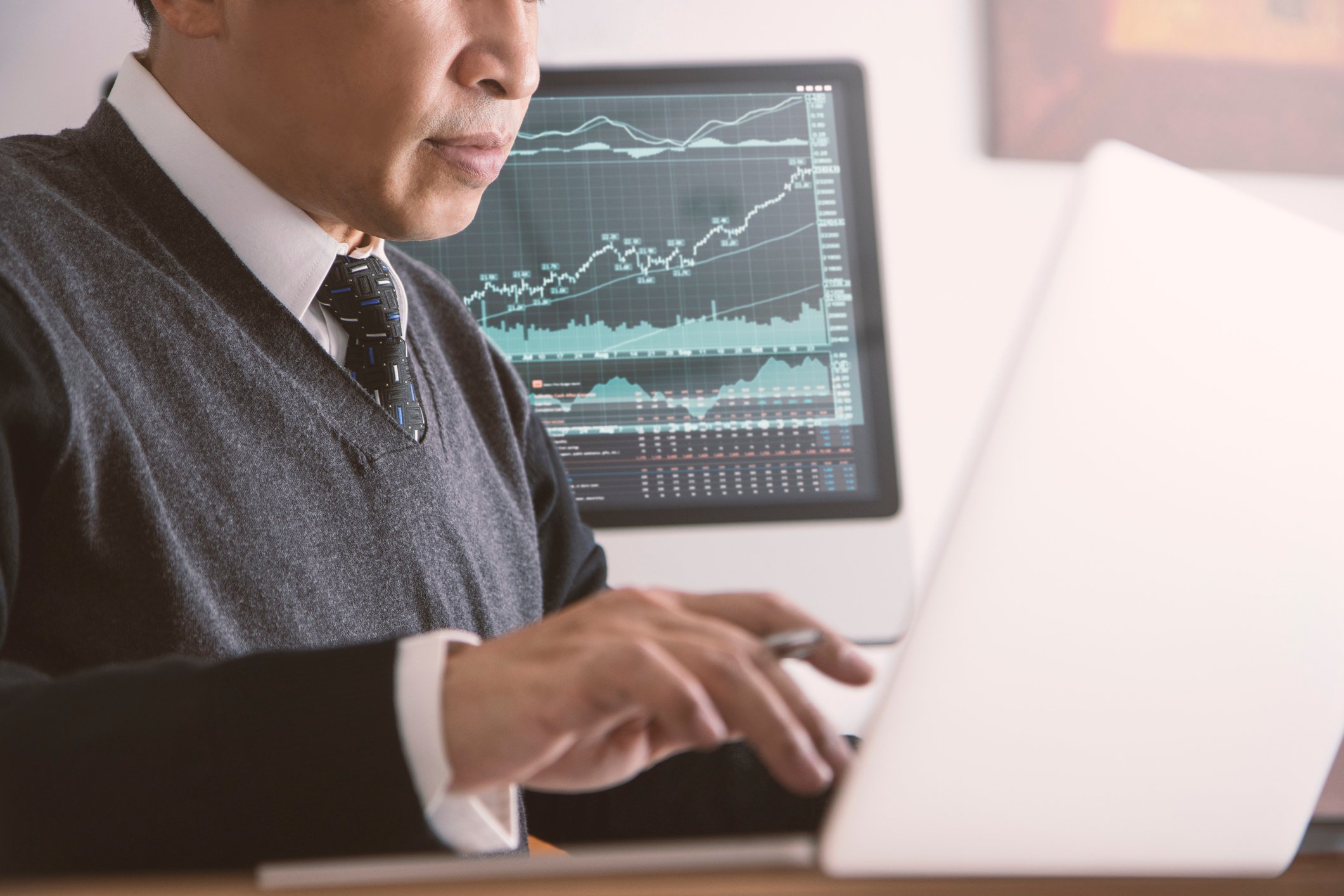 Person looking at laptop with a screen showing a rising stock chart in the background.