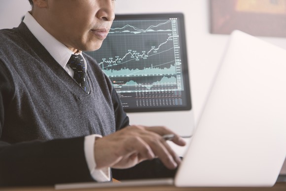 Person looking at laptop with a screen showing a rising stock chart in the background.