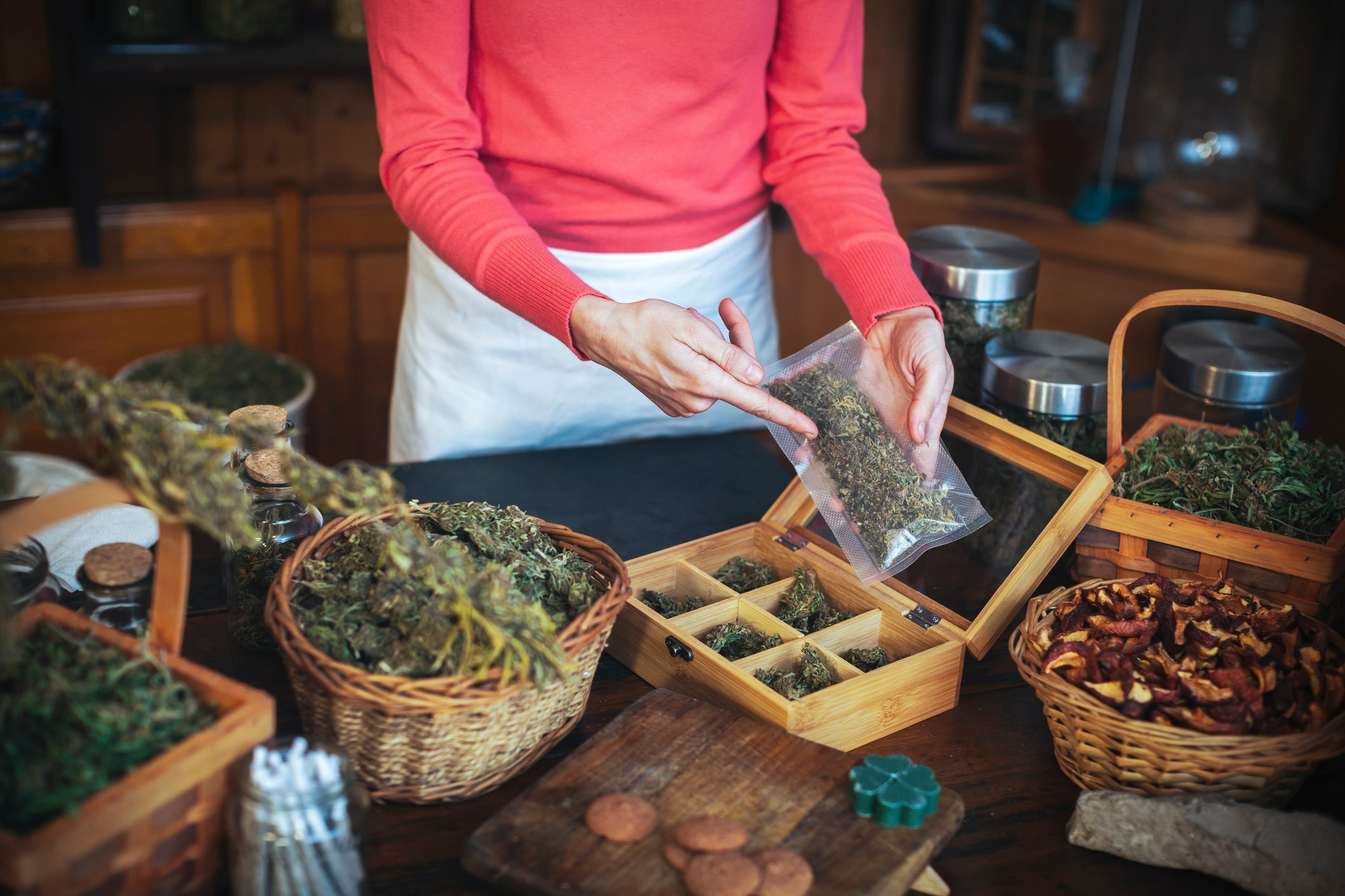 woman points to bags of cannabis in baskets on a table. 