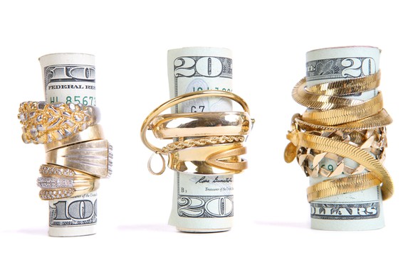A $100 bill and two $20 bills, each wrapped up tightly in gold jewelry, on a white background.