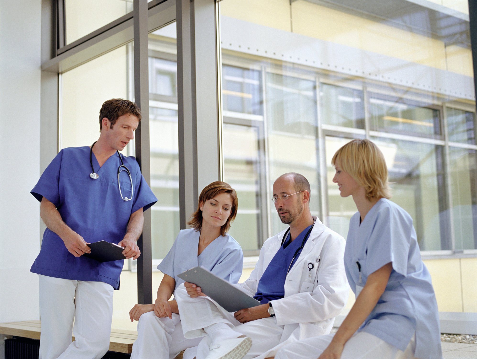 Doctors and nurses looking at a patient chart and talking near a hospital window. 