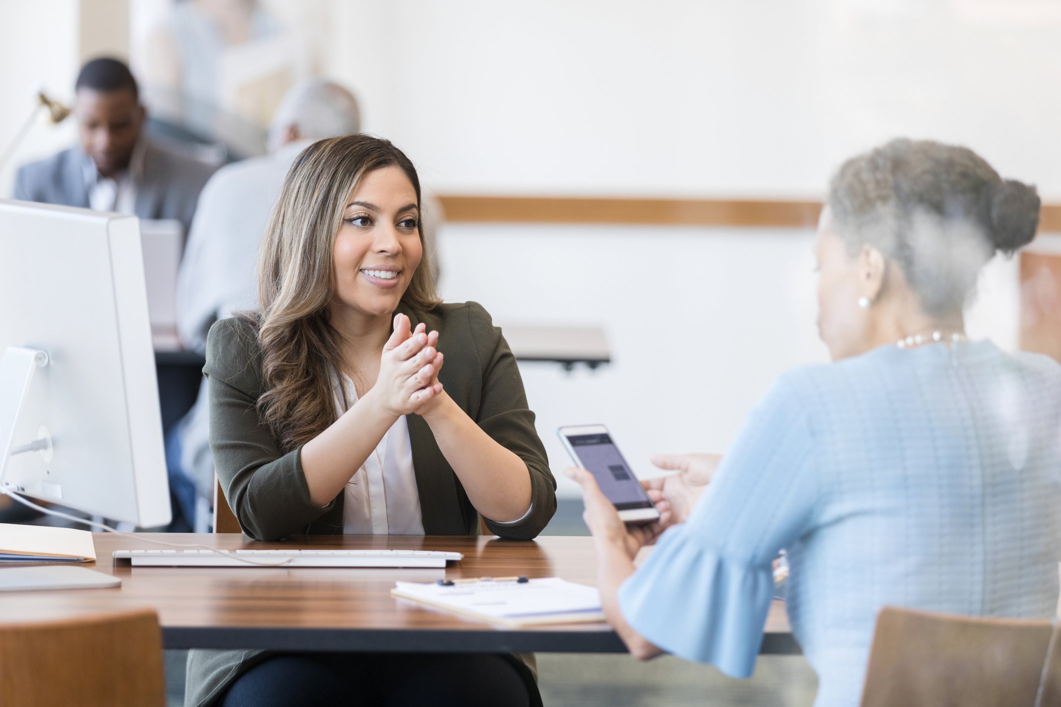 Smiling person across desk from customer holding smartphone with app running.