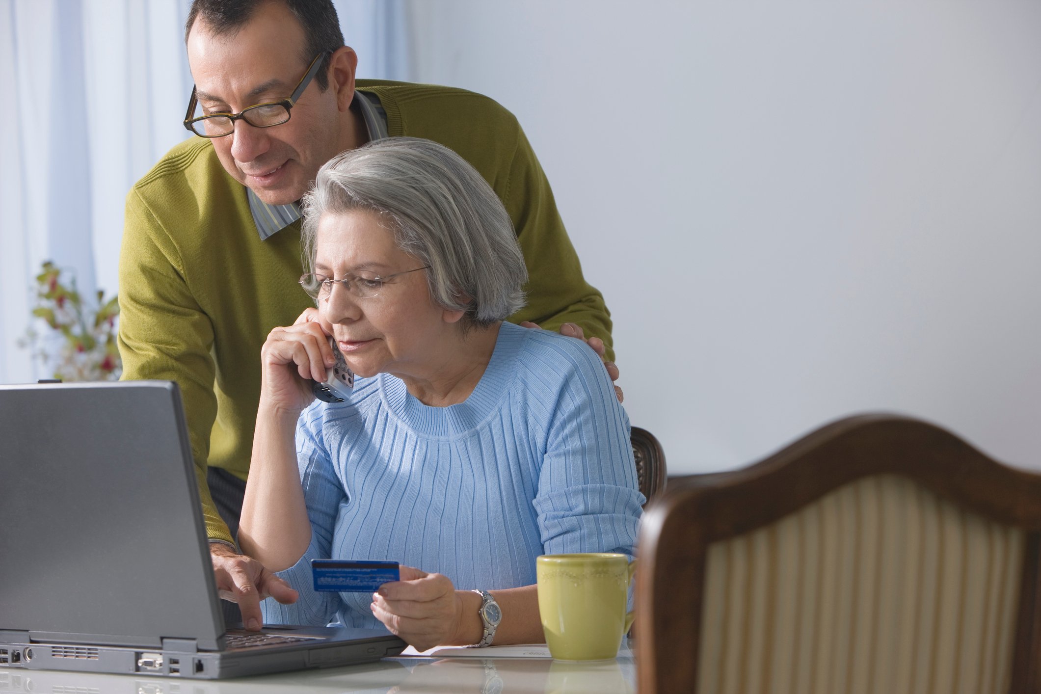 Older couple staring at a laptop at their dining room table while as one of them holds a credit card.