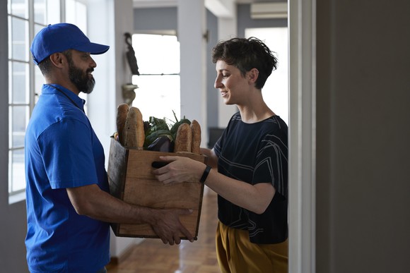 Delivery person gives a box of groceries to a smiling person. 