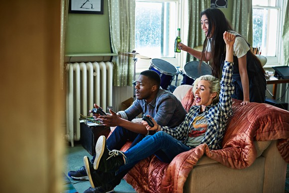 three people in an apartment playing video games and cheering.