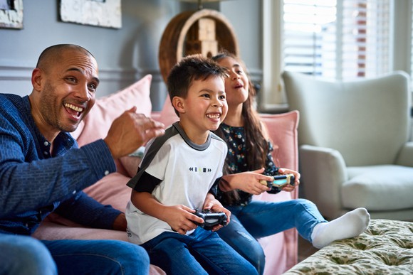 An adult and two children playing video games on a couch.