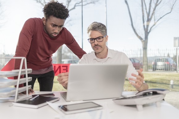 Two men look intently at stock data on a computer screen.
