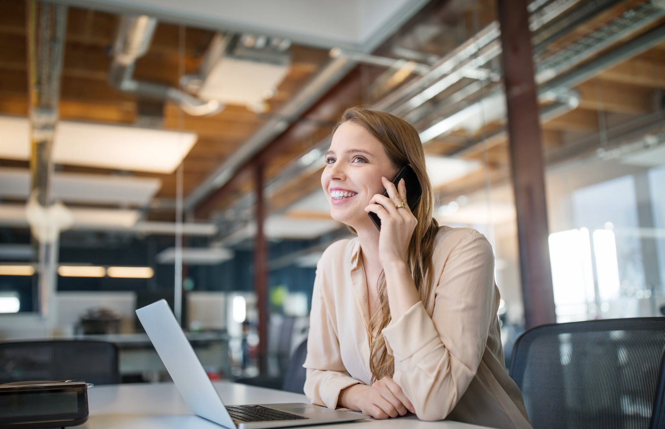 A person on a phone smiling while sitting at computer.