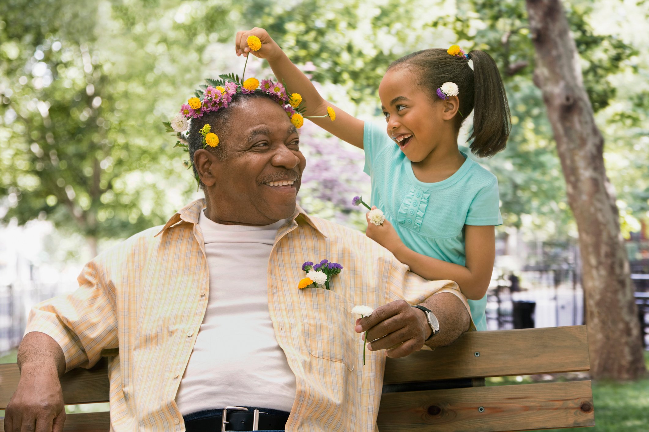 An older person seated on a bench with flowers in their hair, enjoying time spent with the child putting them there.